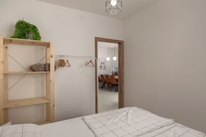 Ein Schlafzimmer mit einem Bett, einem Holzregal mit einer Pflanze, einem Spiegel und einem Essbereich im Hintergrund.