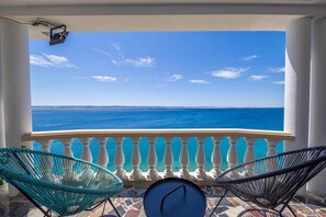 Un balcon avec vue sur la mer, deux chaises et une petite table.