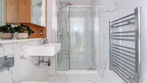 A modern bathroom with a glass shower enclosure, a white sink, and a wooden vanity. - The Ealing Luxury Flat (London)
