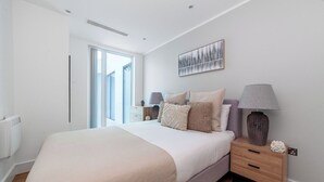 A modern bedroom with a large bed, bedside tables, a window, and a painting on the wall. - The Ealing Luxury Flat (London)