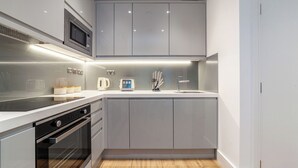 A modern kitchen with grey cabinets, a microwave, a kettle, a toaster, and a sink. - The Ealing Luxury Flat (London)