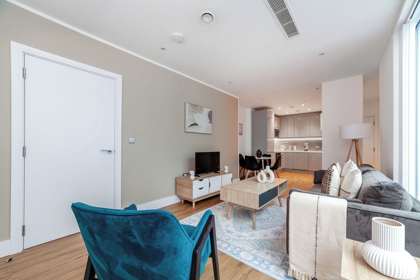Una sala de estar moderna con un sofá, un televisor y una mesa de centro. Se observa una cocina al fondo, con una zona de comedor.