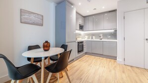 A modern kitchen with grey cabinets, a microwave, and a sink. There is a dining area with a round table and chairs. - The Ealing Luxury Flat (London)