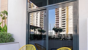 A balcony with two yellow chairs and a small table, a sliding glass door, and a view of a building under construction. - Nasma Holiday Homes - Azizi Riviera 41 (Dubai)