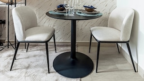 A dining area with a round table, two chairs, a floor lamp, and a patterned wall. - Nasma Holiday Homes - Azizi Riviera 41 (Dubai)