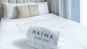 A neatly made bed with a folded towel labeled "NASIMA LUXURY STAYS" and a marble-patterned headboard. - Nasma Holiday Homes - Azizi Riviera 41 (Dubai)