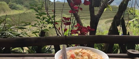 Un plato de comida sobre una mesa de madera con vistas a campos en terrazas y árboles.