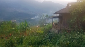 Una casa di legno rustica con un balcone, immersa nel verde e con le montagne sullo sfondo.