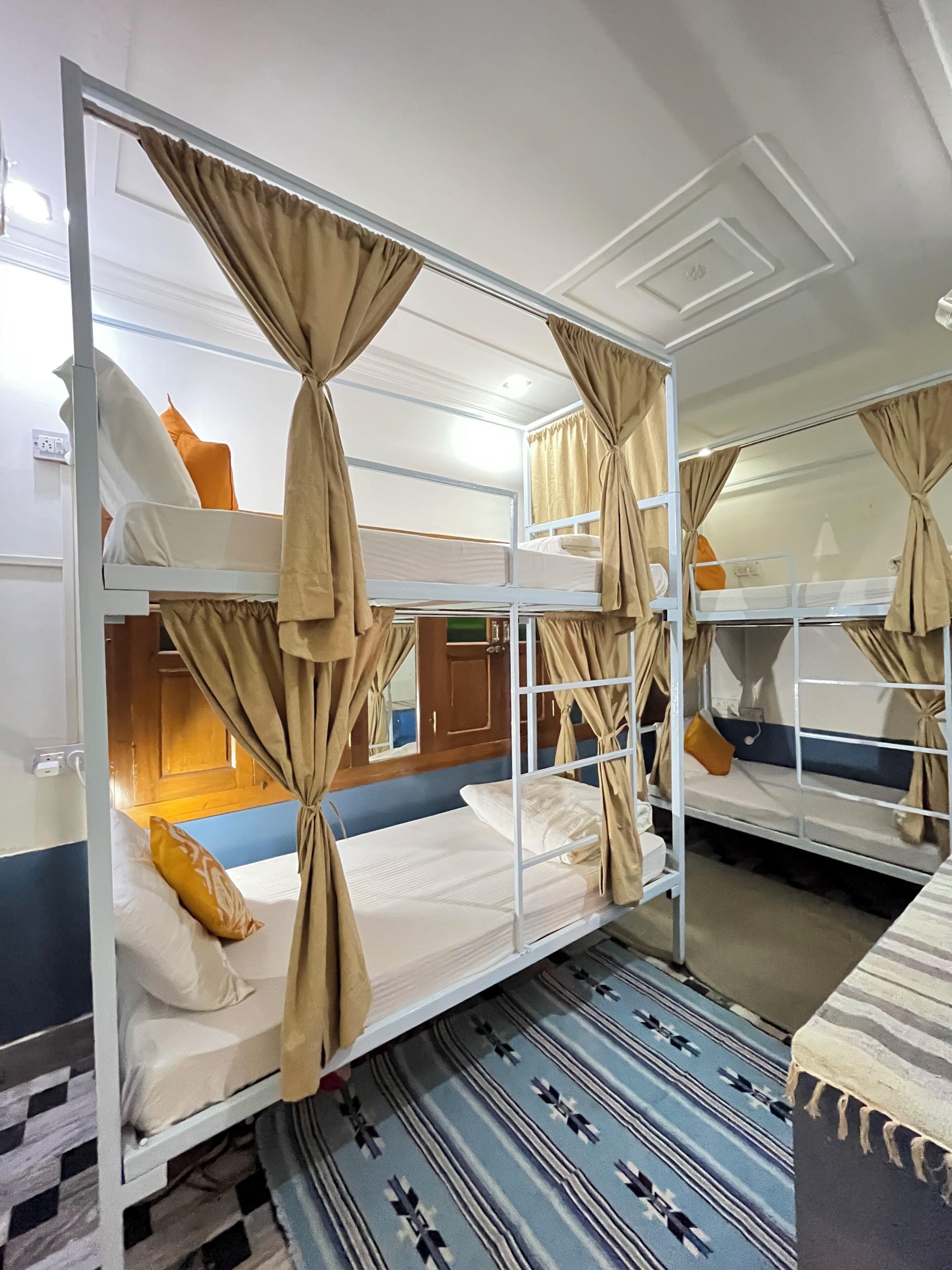 A bunk bed room with curtains tied at the corners, a patterned rug, and a wooden door in the background.