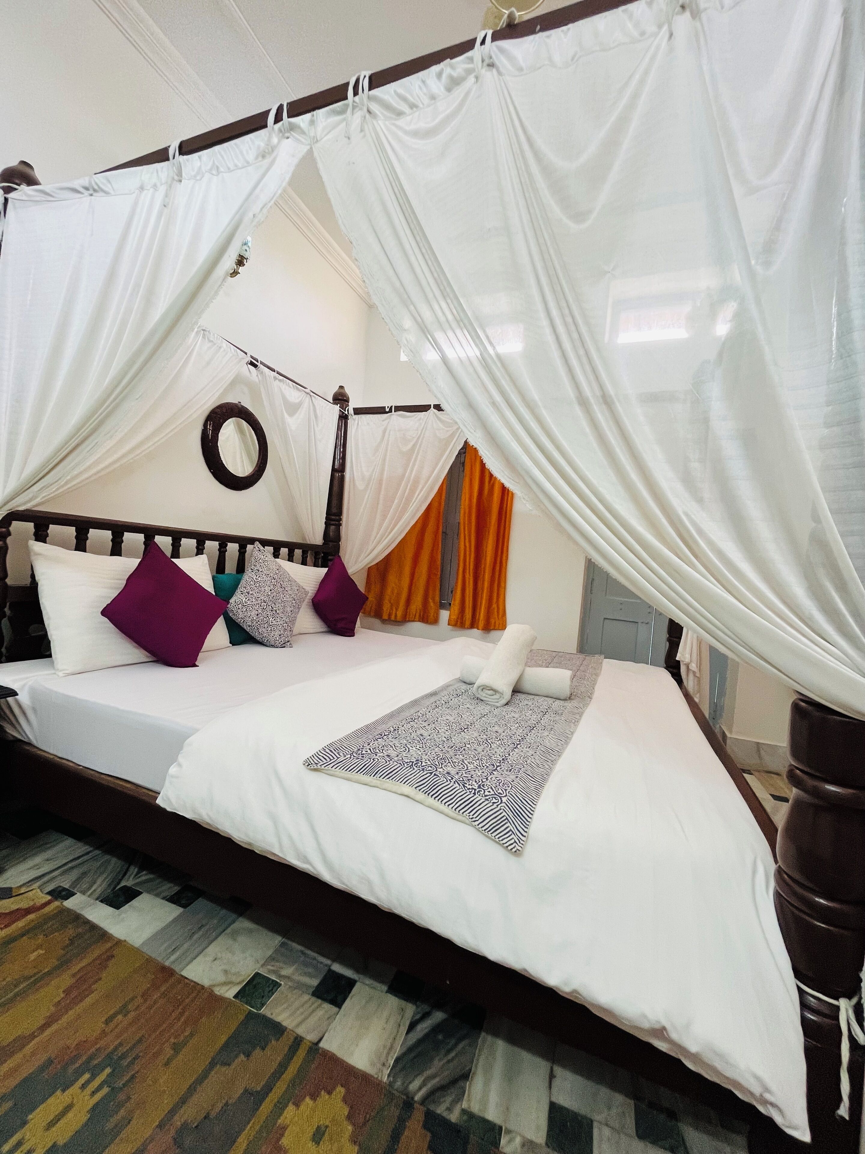 A bed with a canopy, pillows, a patterned rug, and a mirror on the wall.