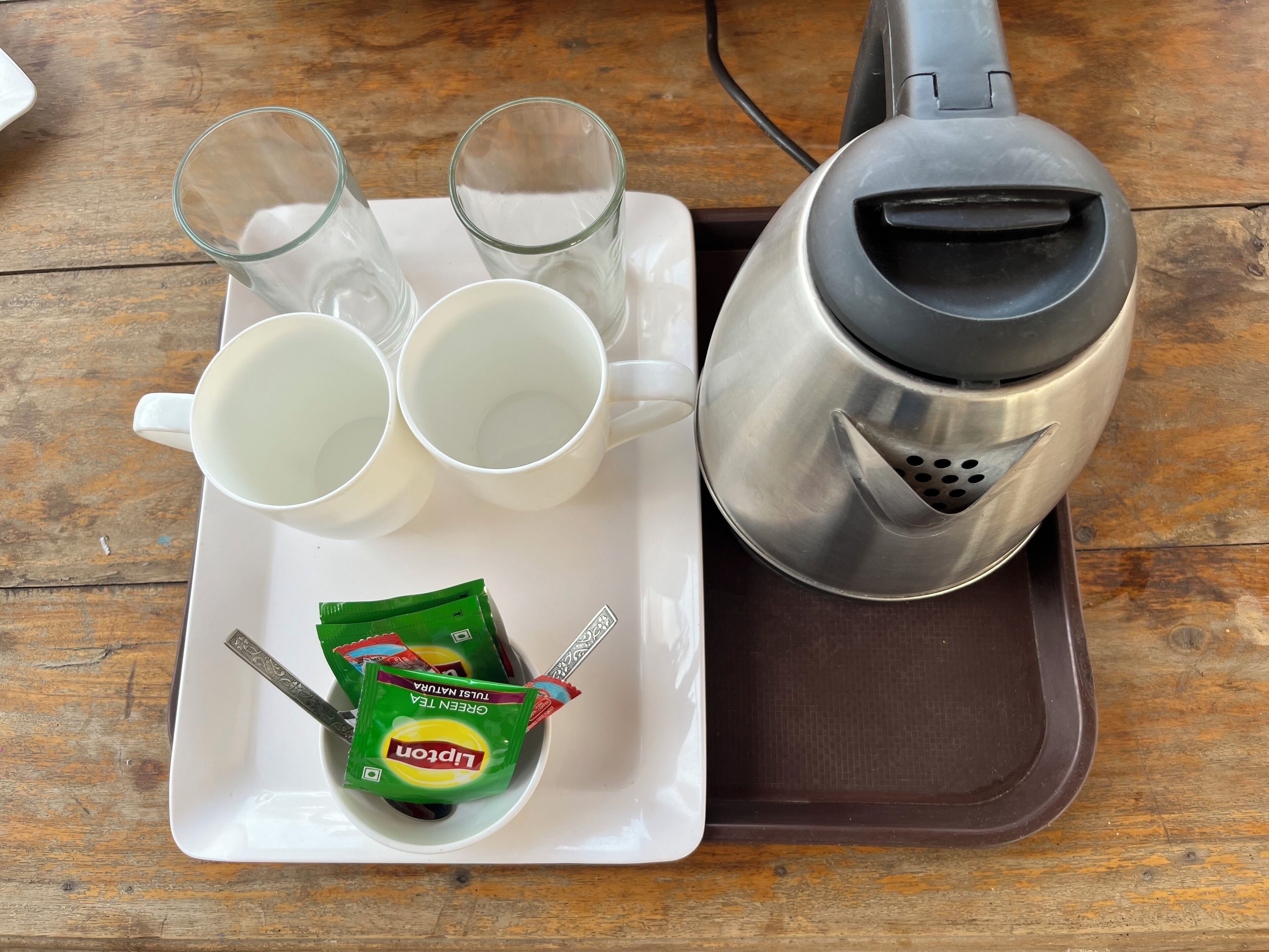 A tray with a coffee maker, two white cups, and a plate with a packet of green tea and a spoon.