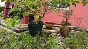 Un edificio rojo con un porche cubierto, plantas en macetas y una motocicleta estacionada afuera.