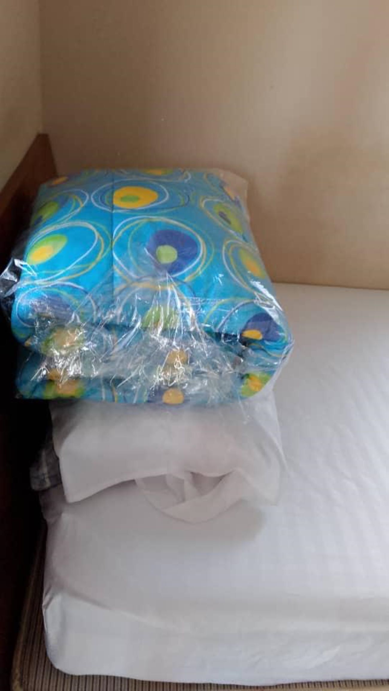 A bed with a white mattress and a pillow wrapped in colorful plastic.
