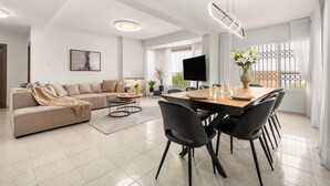 Een moderne woonkamer met een bank, eettafel, stoelen en een televisie.