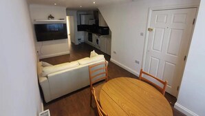 A compact living space with a sofa, a dining table, and a kitchen area. - City Apartment Sleeps 4 With Garden (Romford)
