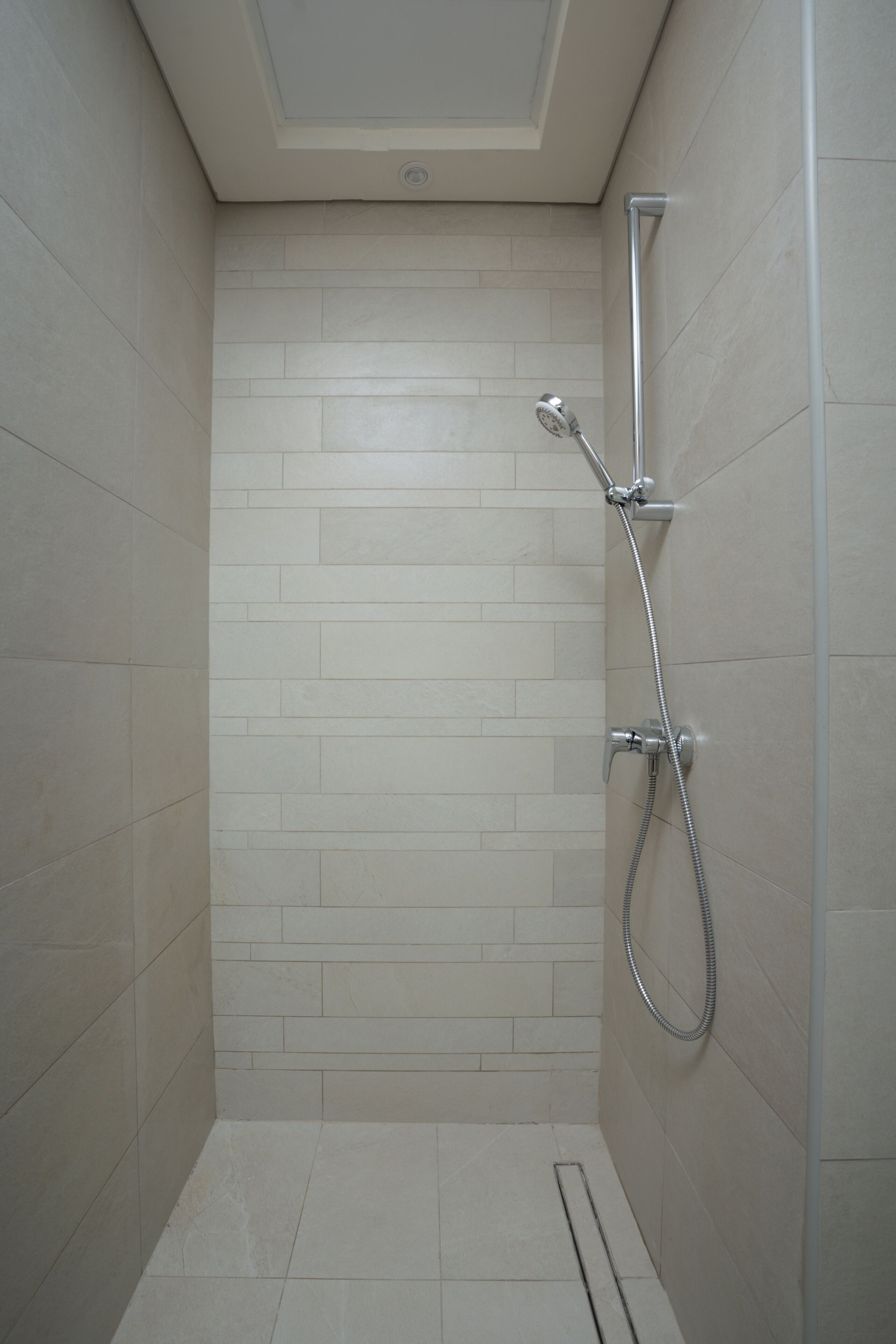 A small, tiled shower room with a handheld showerhead and a wall-mounted faucet.
