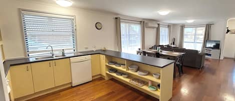 Una cocina compacta con suelo de madera, lavavajillas, comedor con mesa y sillas, y sala de estar con sofá y televisor.