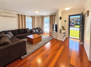 A modern living room with a sectional sofa, a coffee table, and a flat-screen TV. - Boat Access with short Walk to River, Pub and Bowling club. (Harrington)