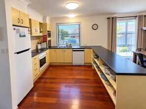 A modern kitchen with wooden flooring, built-in cabinets, a dishwasher, and a window with blinds. - Boat Access with short Walk to River, Pub and Bowling club. (Harrington)