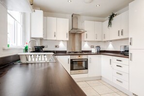 A modern kitchen with white cabinets, a stainless steel range hood, and a built-in oven.