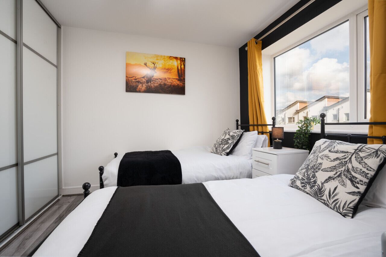 Habitación de hotel con dos camas, un ventanal con cortinas, un cuadro de un ciervo y vistas de edificios.