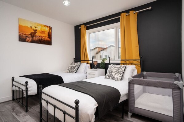 Un dormitorio con dos camas, una ventana con cortinas amarillas, un cuadro de un ciervo y una cuna.