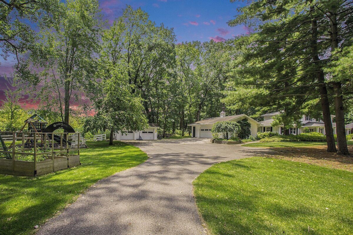 A residential area with a paved driveway leading to a row of houses, surrounded by lush greenery and trees.