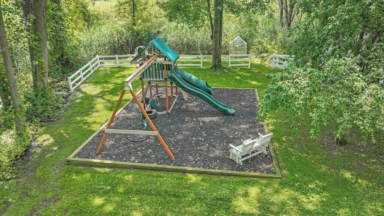 Un parque infantil con tobogán y estructura de escalada, rodeado de césped y árboles.