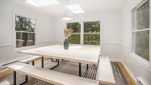 A bright, white room with a large table and benches, large windows, and a skylight. - Klinger Lake Cove - Sleeps 16-24 (White Pigeon)