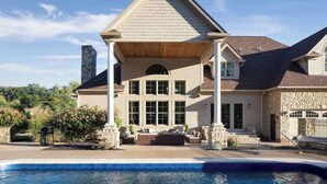 Une grande maison à deux étages, avec une façade en pierre, une cheminée imposante et un patio couvert.