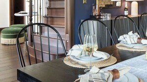Un coin repas avec une table en bois foncé, dressée pour quatre personnes, un escalier et un miroir au mur.