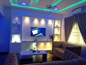Una sala de estar moderna con un televisor de pantalla plana montado en la pared, un sofá, una mesa de centro y un ventilador de techo.