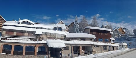 Un edificio cubierto de nieve con fachada de piedra, múltiples ventanas y cielo despejado.