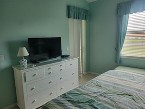 A bedroom with a bed, a TV on a dresser, a lamp, and a window with curtains.