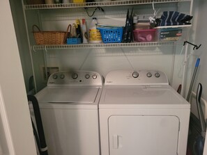 Een wasserette met twee Whirlpool wasmachines en drogers, planken met schoonmaakmiddelen en een mand.