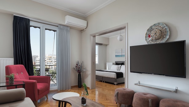 A modern living room with a red armchair, a beige sofa, a small round table, and a TV on the wall. - Athenian Heritage Residences (Athens)