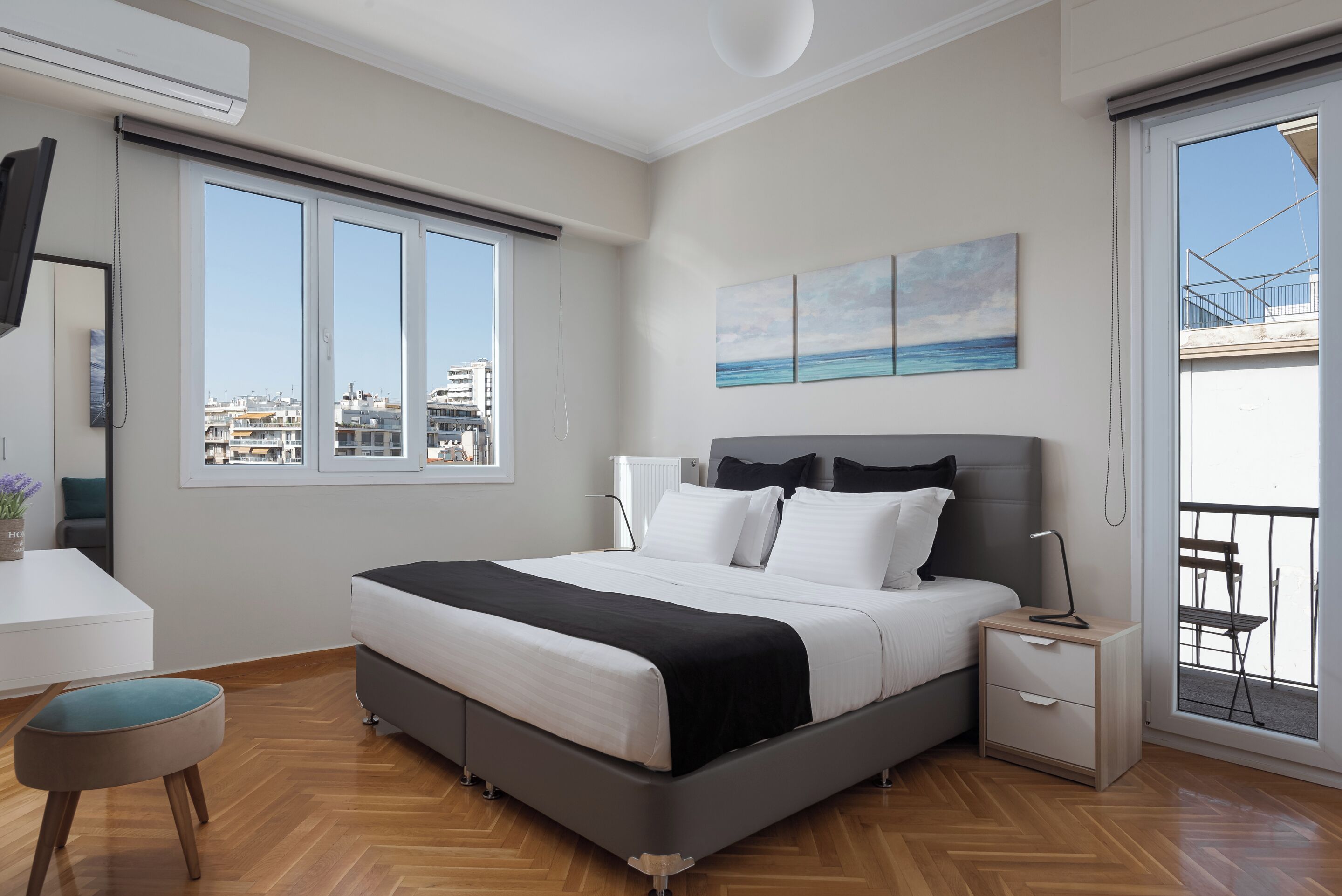 A modern bedroom with a large bed, bedside tables, a desk, and a view of the city through large windows.