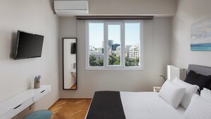 A modern bedroom with a bed, a TV, a window with a city view, and a radiator. - Athenian Heritage Residences (Athens)