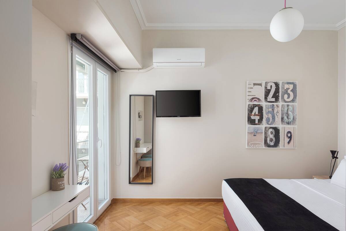 Une chambre à coucher avec un lit, un téléviseur fixé au mur, un miroir et une fenêtre donnant sur l’extérieur.