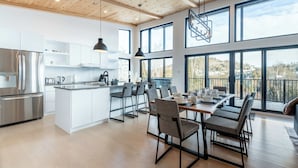 A modern kitchen with white cabinetry, a stainless steel refrigerator, and a dining area with a large island and multiple chairs. - Spa & Mountain View | Le Eastmain View (Saint-Côme)