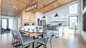A modern kitchen with white cabinets, a central island, and pendant lighting. - Spa & Mountain View | Le Eastmain View (Saint-Côme)