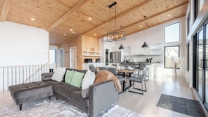A modern interior with a wooden ceiling, a grey sectional sofa, a dining area, and a kitchen. - Spa & Mountain View | Le Eastmain View (Saint-Côme)
