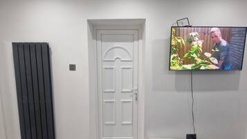 A room with a white door, a radiator, and a television mounted on the wall.