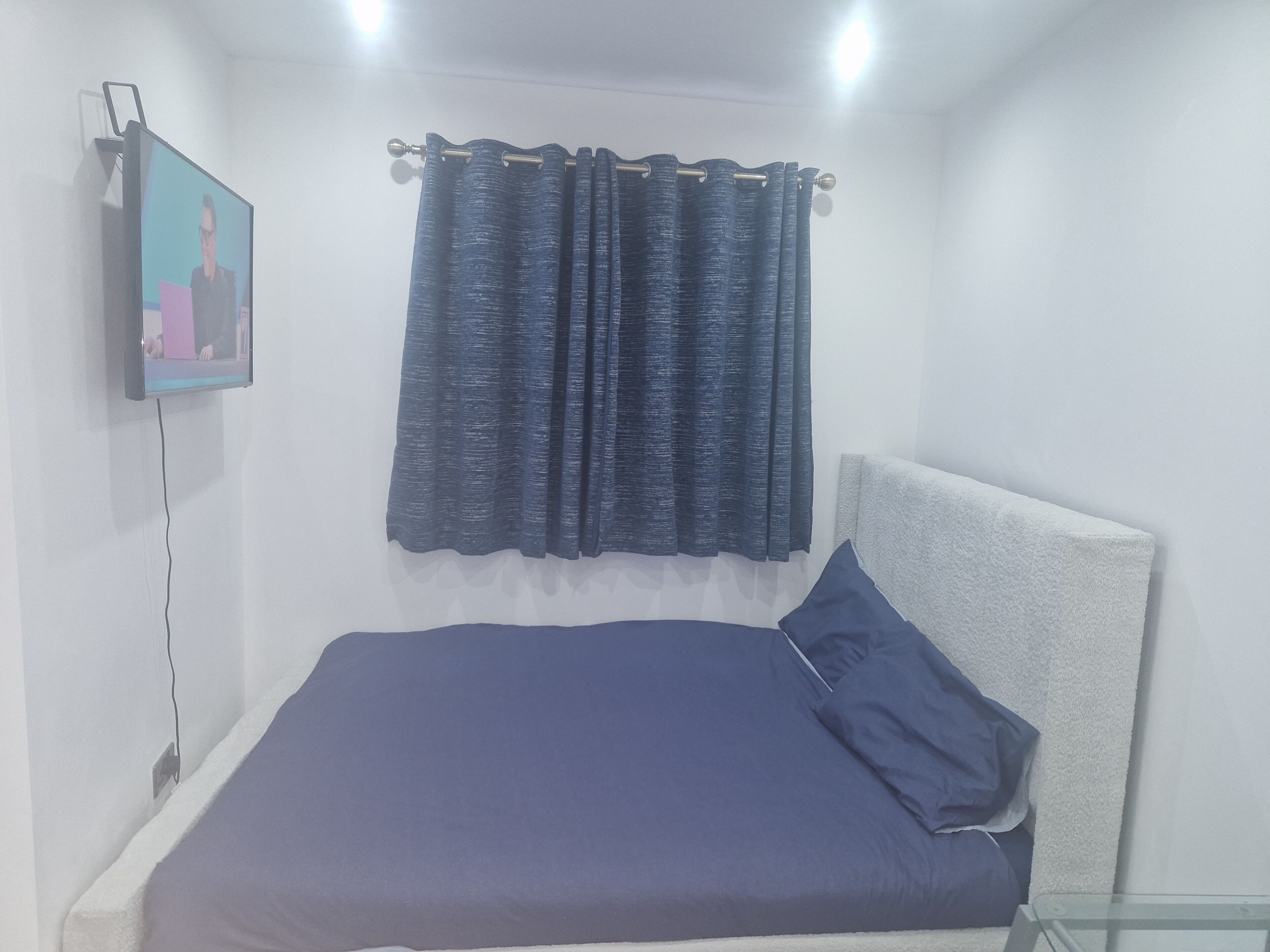 A bedroom with a bed, a TV mounted on the wall, and a curtain.
