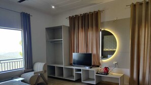 Ein modernes Hotelzimmer mit einem Bett, einem Fernseher auf einem weißen Schrank, einem runden Spiegel und Blick auf einen Balkon.
