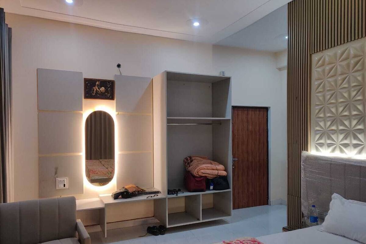 A modern hotel room with a bed, a seating area, a vanity with a mirror, and built-in shelving.