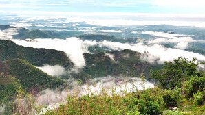 Ein weitreichender Panoramablick auf eine gebirgige Landschaft mit üppiger Vegetation und vereinzelten Wolken.
