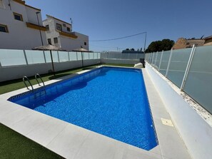 Ein rechteckiger Swimmingpool mit klarem, blauem Wasser, umgeben von einer weißen Fliesenveranda und einer Glasumrandung.