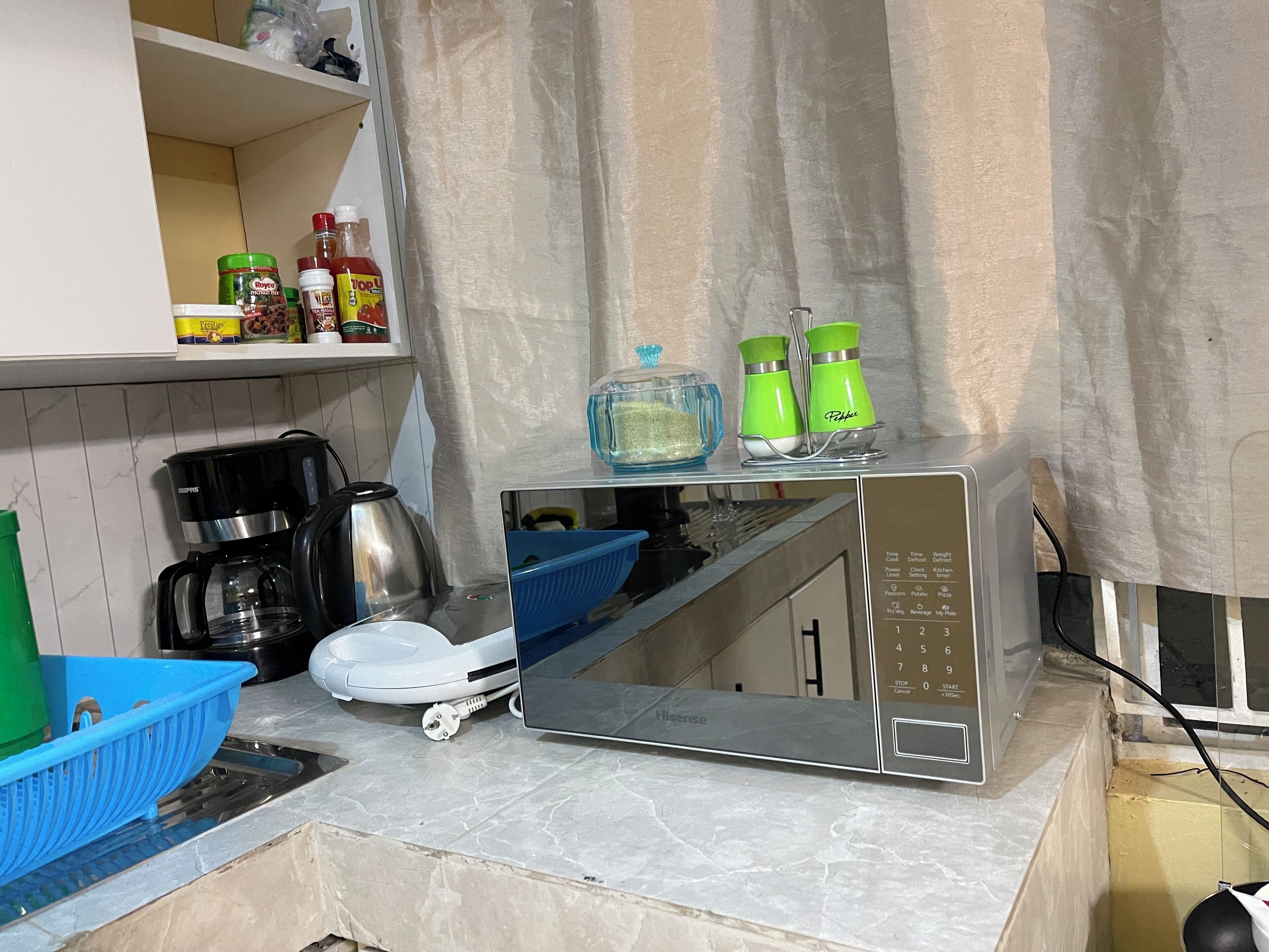 A compact kitchen with a microwave, a coffee maker, and a blue colander on the counter.