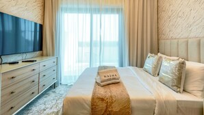 A hotel room with a bed, a TV on a wooden dresser, and a window with curtains. - Nasma Holiday Homes - Azizi Riviera 46 (Dubai)